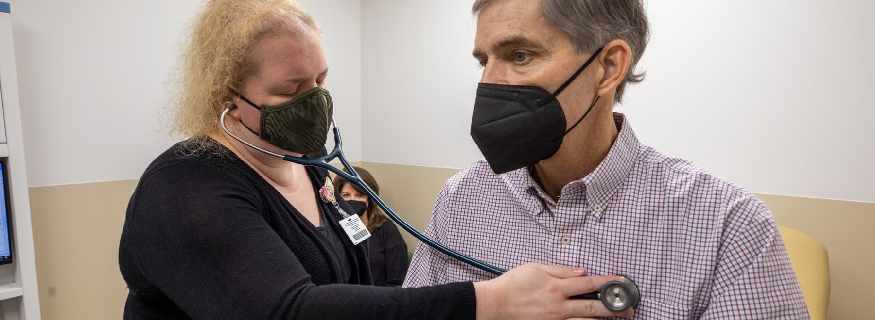 Woman listening to heartbeat of man in mask.